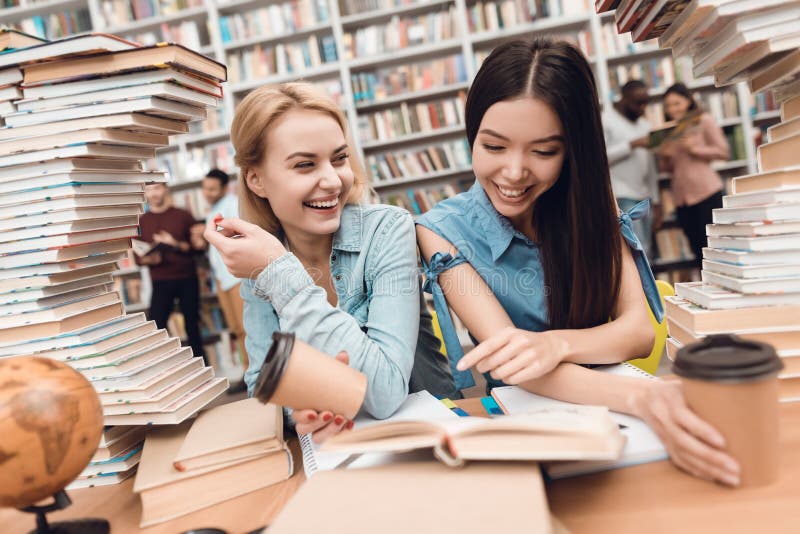 Ethnic asian girl and white girl surrounded by books in library. Students are reading book.