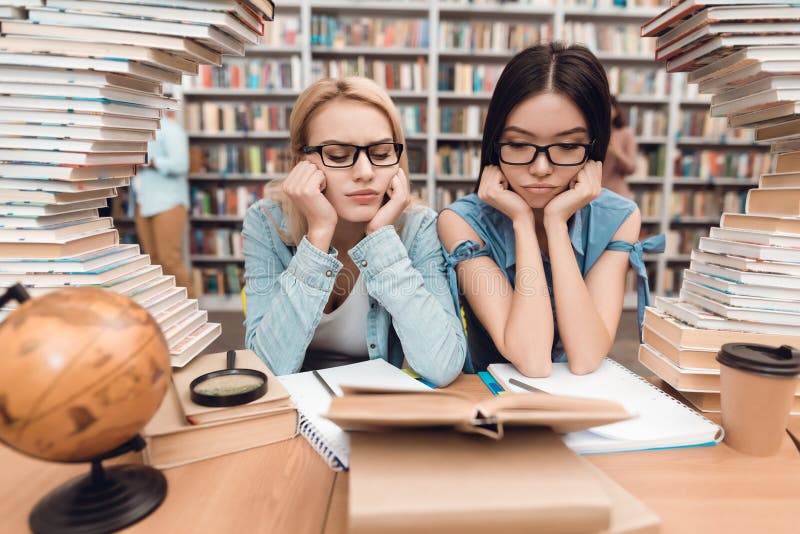 Ethnic asian girl and white girl surrounded by books in library. Students are reading book.