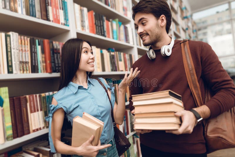 Ethnic asian girl and white guy in library. Students are looking for books.