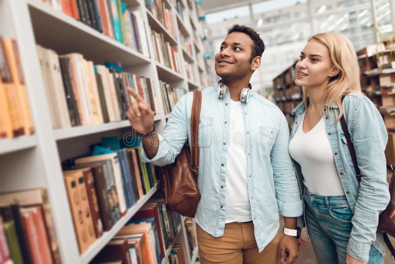 Ethnic indian mixed race guy and white girl in library. Students are looking for books.