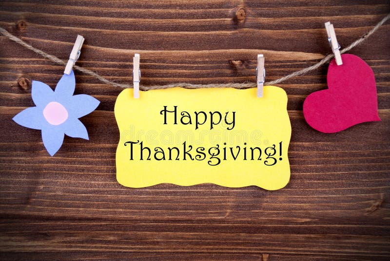 Happy Thanksgiving Greetings on a Yellow Label with a Flower and a Heart Symbol Hanging on a Line. Happy Thanksgiving Greetings on a Yellow Label with a Flower and a Heart Symbol Hanging on a Line