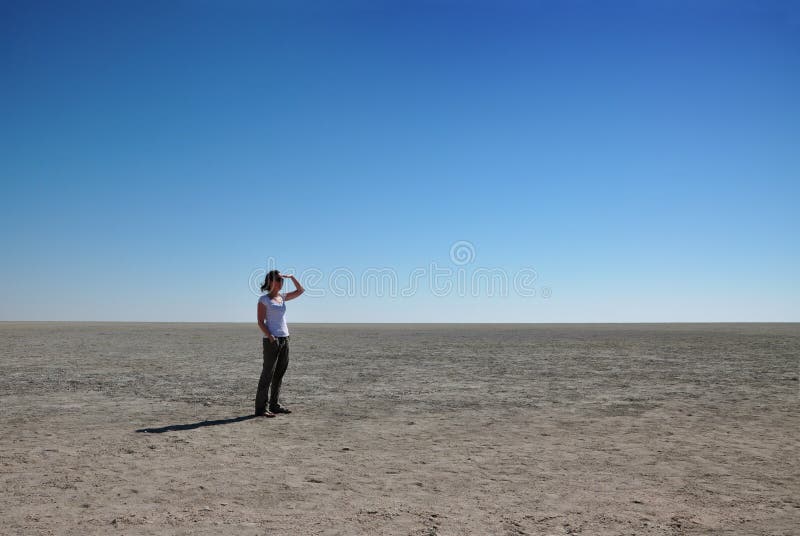 Lonely woman looking out over an endless salt pan in Etosha National Park, Namibia. Lonely woman looking out over an endless salt pan in Etosha National Park, Namibia.