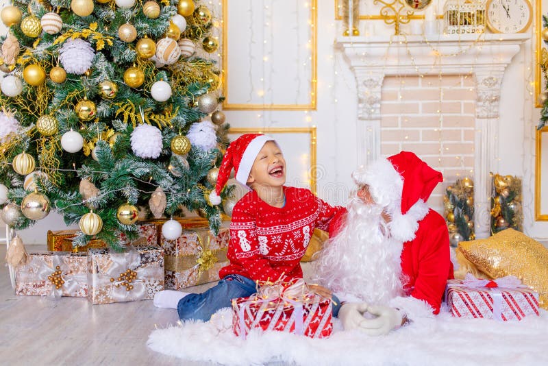 Ett barn och julklaus skrattar nära julgranen... ett lyckligt barn pratar med Santa claus. arkivfoto