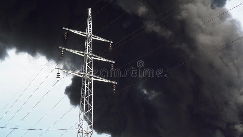 An electric tower stands against a background of black smoke. A big chemical fire at a factory building. Thick black smoke covers the sky. 4k. An electric tower stands against a background of black smoke. A big chemical fire at a factory building. Thick black smoke covers the sky. 4k