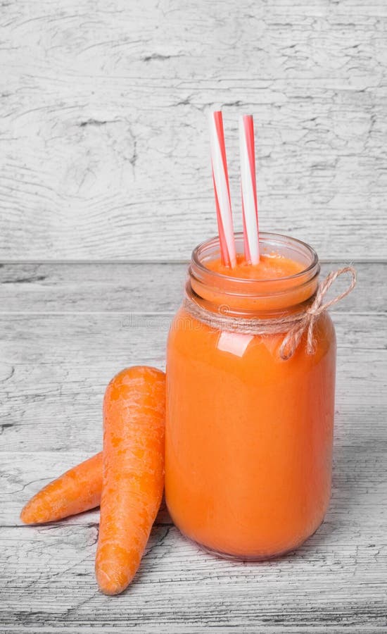 Ett exponeringsglas av den morotmilkshake eller smoothien med att dricka sugrör på en ljus träbakgrund, närbild fotografering för bildbyråer Ett exponeringsglas av den morotmilkshake eller smoothien med att dricka sugrör på en ljus träbakgrund, närbild fotografering för bildbyråer