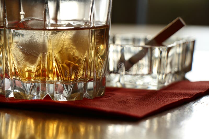 Ett exponeringsglas av whisky på vaggar och en röka cigarett royaltyfria bilder Ett exponeringsglas av whisky på vaggar och en röka cigarett royaltyfria bilder