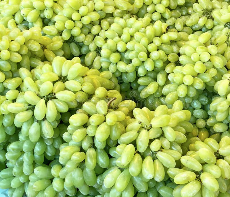 a photography of a bunch of green grapes are piled together, woollen grapes are piled on a blue plate in a market. a photography of a bunch of green grapes are piled together, woollen grapes are piled on a blue plate in a market.
