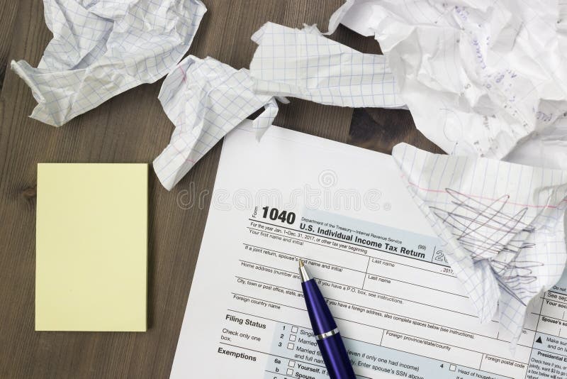 Ett foto från ovannämnt av den USA IRS skattformen 1040, gulinganmärkningar, skrynklade pappers- ark och en penna på trätabellen royaltyfria bilder Ett foto från ovannämnt av den USA IRS skattformen 1040, gulinganmärkningar, skrynklade pappers- ark och en penna på trätabellen royaltyfria bilder