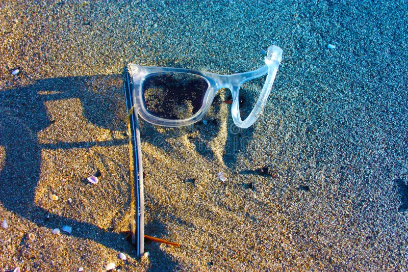 Ett gammalt par av övergett vitt och genomskinligt plast- glasögon lämnade bara på den sandiga stranden brutna objekt och luftför arkivfoto Ett gammalt par av övergett vitt och genomskinligt plast- glasögon lämnade bara på den sandiga stranden brutna objekt och luftför arkivfoto