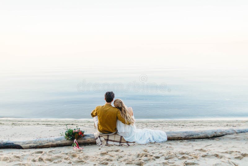 Ett härligt par sitter på journalen och blicken till havet Romantiskt datum på stranden tillbaka sikt bröllop arkivbilder Ett härligt par sitter på journalen och blicken till havet Romantiskt datum på stranden tillbaka sikt bröllop arkivbilder