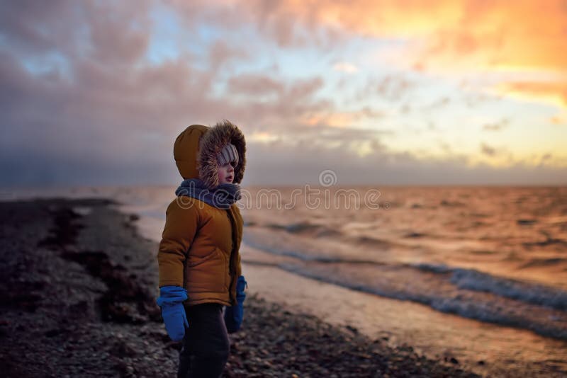 Ett litet barn går på Östersjöns kust vid solnedgången på vinterdagen Utomhusaktiviteter för familj med barn på vintern arkivfoto