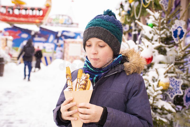 joyful 9 year old boy on a christmas holiday on a snowy day, holding churos donuts in his hands. joyful 9 year old boy on a christmas holiday on a snowy day, holding churos donuts in his hands