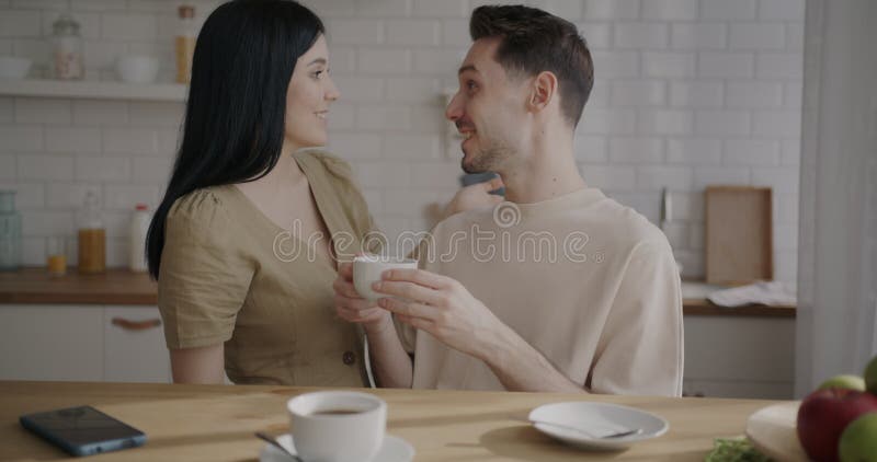 Ett lyckligt ungt par som dricker kaffe pratar och uttrycker kärlek i köket i lägenheten