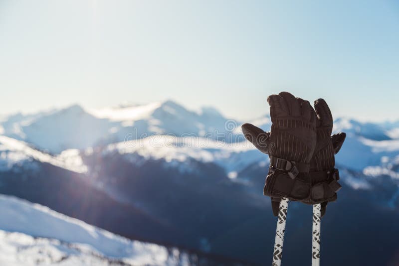 Ett par av skidar handskar på poler med snöig bergmaxima i bakgrunden på en solig dag arkivfoton Ett par av skidar handskar på poler med snöig bergmaxima i bakgrunden på en solig dag arkivfoton