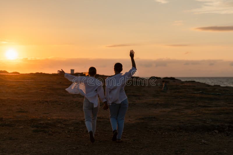 Ett par solnedgångstrand går två personer i vita kläder hand mot solnedgången på en strand. royaltyfri foto