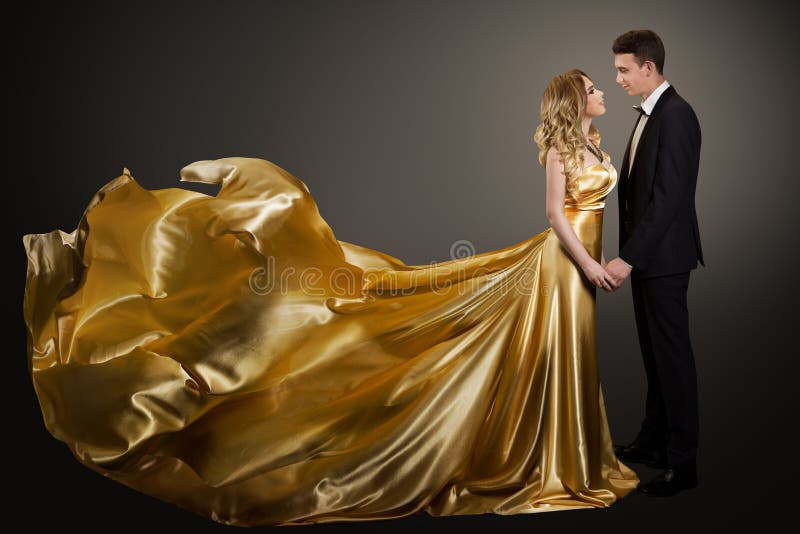 Ett par, vackra kvinnor i Golden Silk Dress och Elegant Man, Fluttering Gown royaltyfri foto