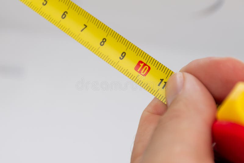 Ett slut upp av en gul metermåttband med en vit hand som rymmer den nära för precision arkivfoton