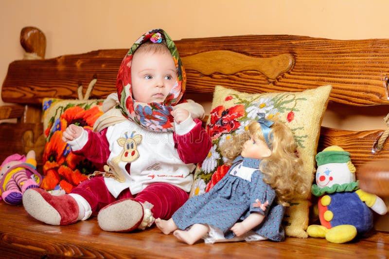 Ett småbarn i ett sjalsammanträde på en soffa med broderade kuddar royaltyfri bild Ett småbarn i ett sjalsammanträde på en soffa med broderade kuddar royaltyfri bild