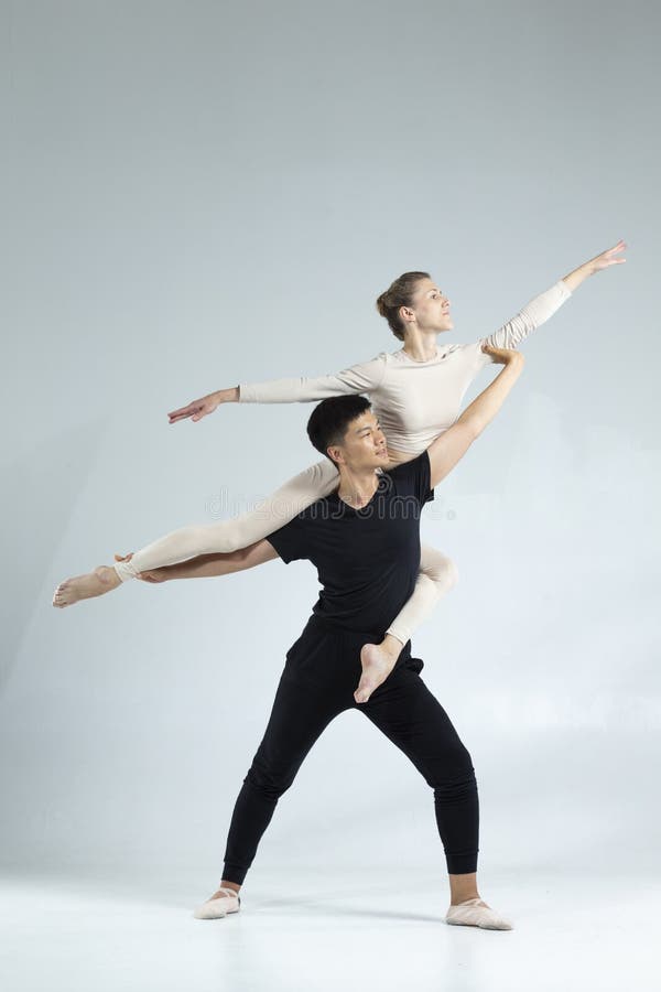 Ett sportiskt par asisk man och kaukasisk kvinna som utför balettdansare över grått i studio under uppskov i klassisk royaltyfri foto