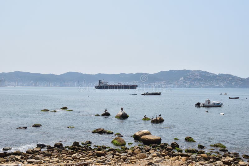A large ship is sailing in the ocean near a rocky shore. The water is calm and the sky is clear in Acapulco Mexico. A large ship is sailing in the ocean near a rocky shore. The water is calm and the sky is clear in Acapulco Mexico