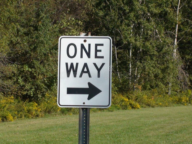 A One Way Sign with trees and freshly cut grass. A One Way Sign with trees and freshly cut grass.
