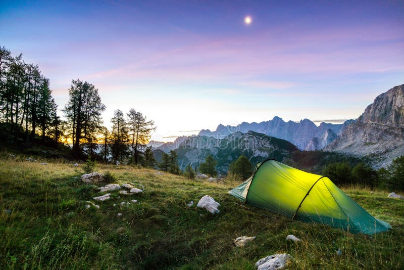 Ett tält glöder under en månenatthimmel på skymningtimmen Fjällängar Triglav nationalpark, Slovenien royaltyfria foton Ett tält glöder under en månenatthimmel på skymningtimmen Fjällängar Triglav nationalpark, Slovenien royaltyfria foton