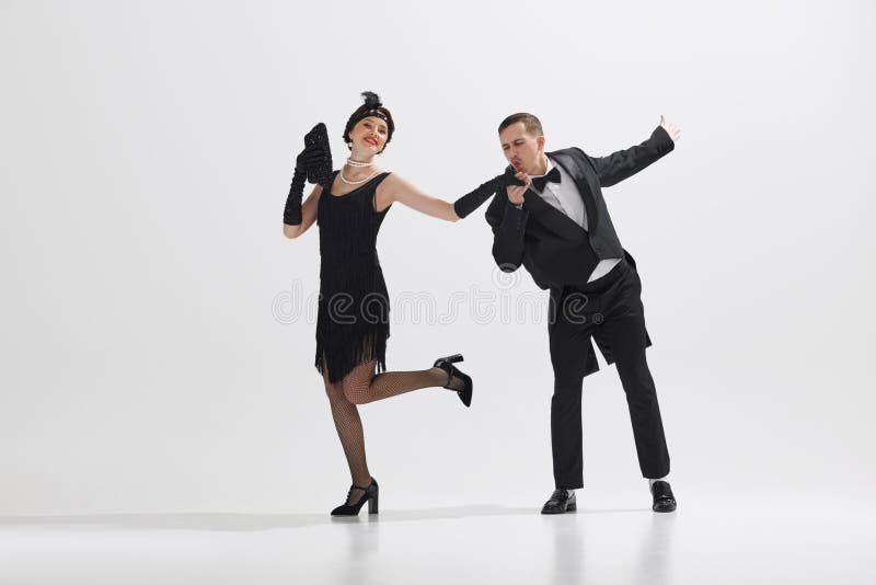 Young couple styled in 1920s fashion, elegant men and women dancing isolated against white studio background. Concept of art, retro and vintage, hobby, entertainment, 20s. Young couple styled in 1920s fashion, elegant men and women dancing isolated against white studio background. Concept of art, retro and vintage, hobby, entertainment, 20s