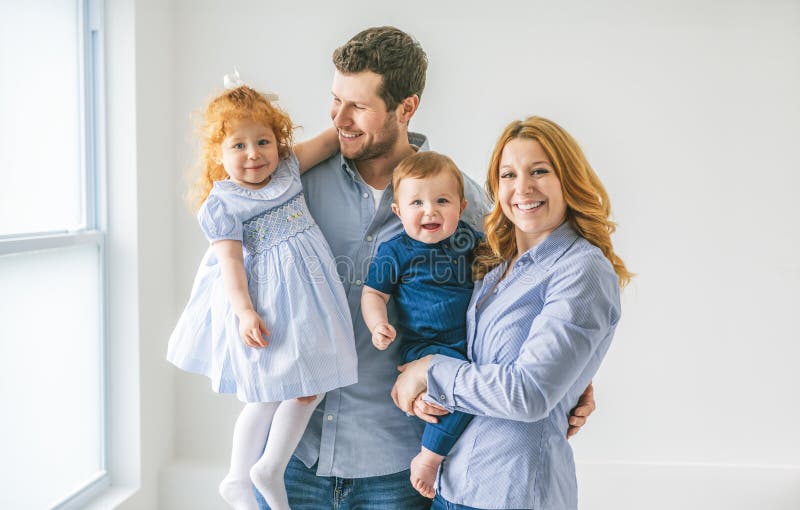 Ett ungt, vackert familjepar med babypojke och två års dotter med grå studio arkivbild