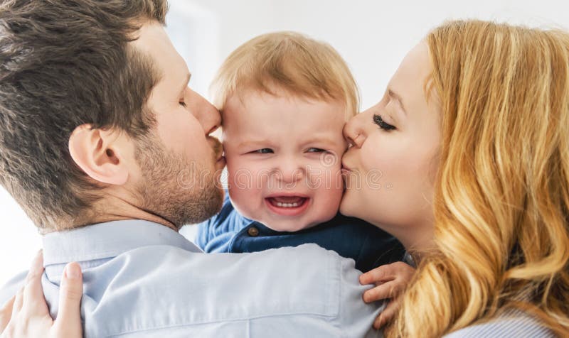 Ett ungt, vackert familjepar som tröstar babypojken på grå studio arkivfoto