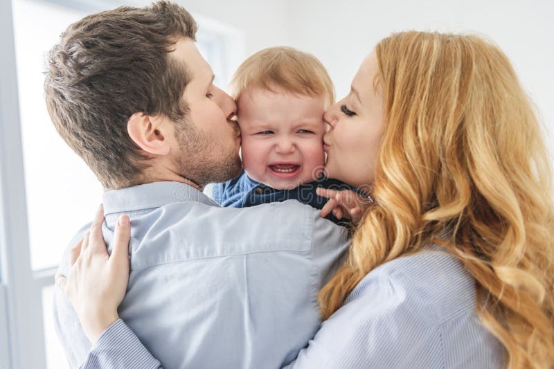 Ett ungt, vackert familjepar som tröstar babypojken på grå studio fotografering för bildbyråer