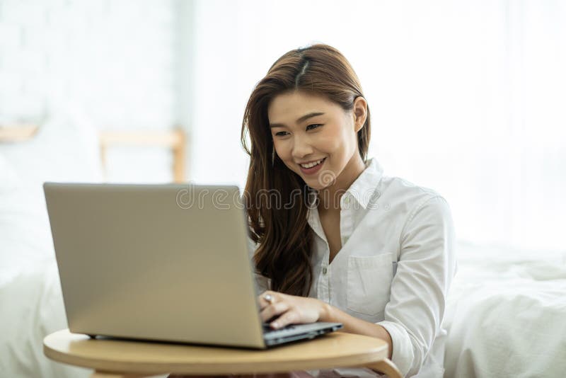 Ett vackert sätt att leva som en vacker kvinna som leker när hon arbetar eller handlar online med en bärbar dator i sovrummet arkivbild