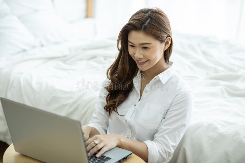 Ett vackert sätt att leva som en vacker kvinna som leker när hon arbetar eller handlar online med en bärbar dator i sovrummet arkivbilder