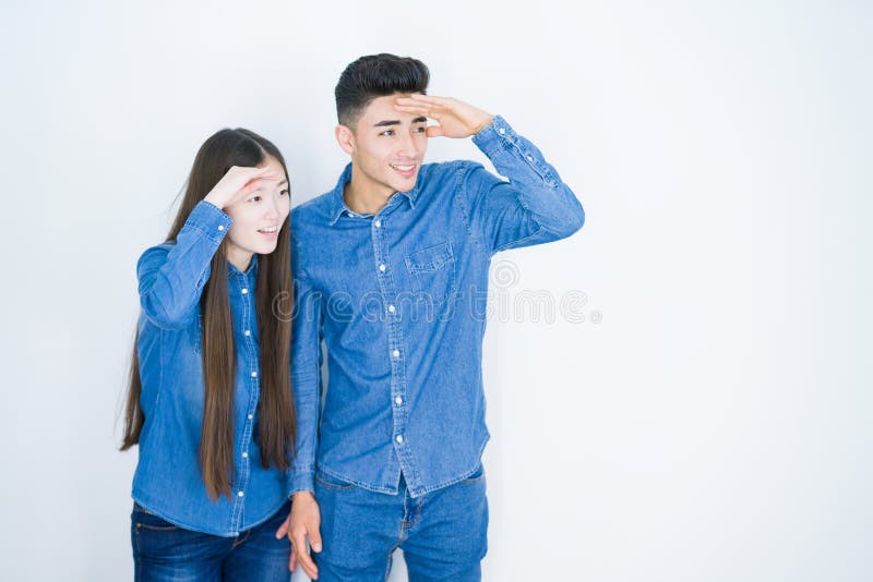 Ett vackert, ungt asianskt par över vit, isolerad bakgrund mycket glad och leende som ser långt bort med hand över huvudet arkivfoto