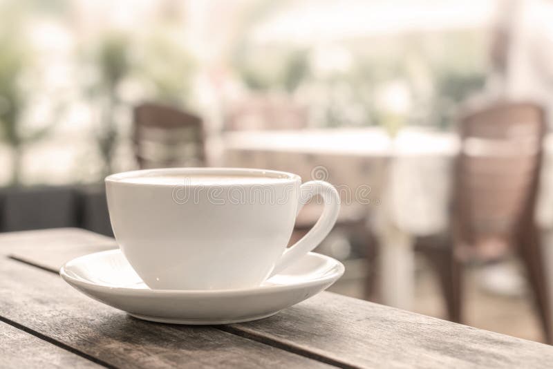 Ett vitt kaffe rånar står på en trätabell i en utomhus- coffee shop Ljus suddig bakgrund close upp arkivfoto Ett vitt kaffe rånar står på en trätabell i en utomhus- coffee shop Ljus suddig bakgrund close upp arkivfoto