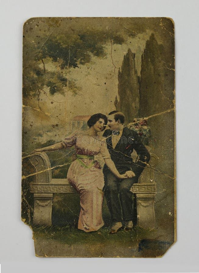 Vintage postcard, a beautiful girl and a young man sitting in a park on a stone bench among flowers. Sepia. The filming time is around 1915. Vintage photography circa 1915. Vintage postcard, a beautiful girl and a young man sitting in a park on a stone bench among flowers. Sepia. The filming time is around 1915. Vintage photography circa 1915