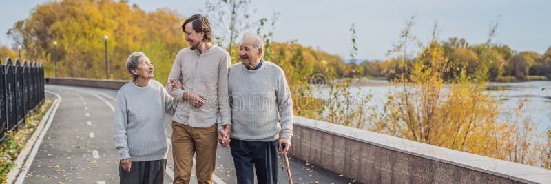 Ett äldre par går i parkerar med en manlig assistent eller en vuxen sonson Att bry sig för det äldre och att ställa upp som frivi royaltyfri fotografi