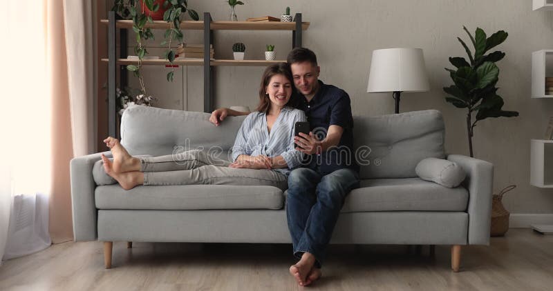 Ett årtusende par som slappnar på soffan med smartphone lager videofilmer
