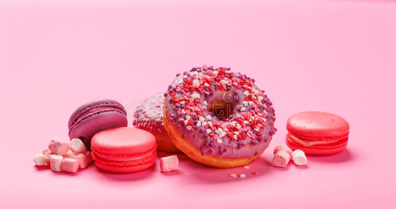 Ett ögonetsarrangemang med färgade makaroner och donötter på en pastellrosa bakgrund fotografering för bildbyråer
