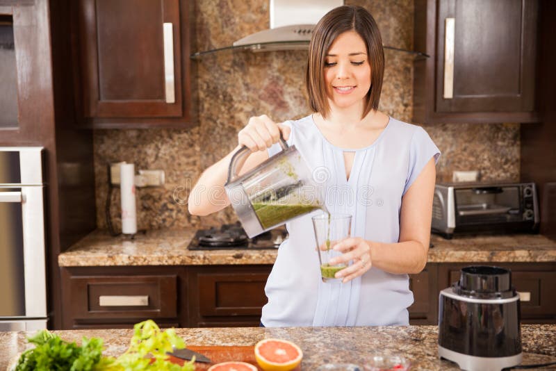 Pretty young Hispanic woman serving some freshly made green juice for breakfast. Pretty young Hispanic woman serving some freshly made green juice for breakfast