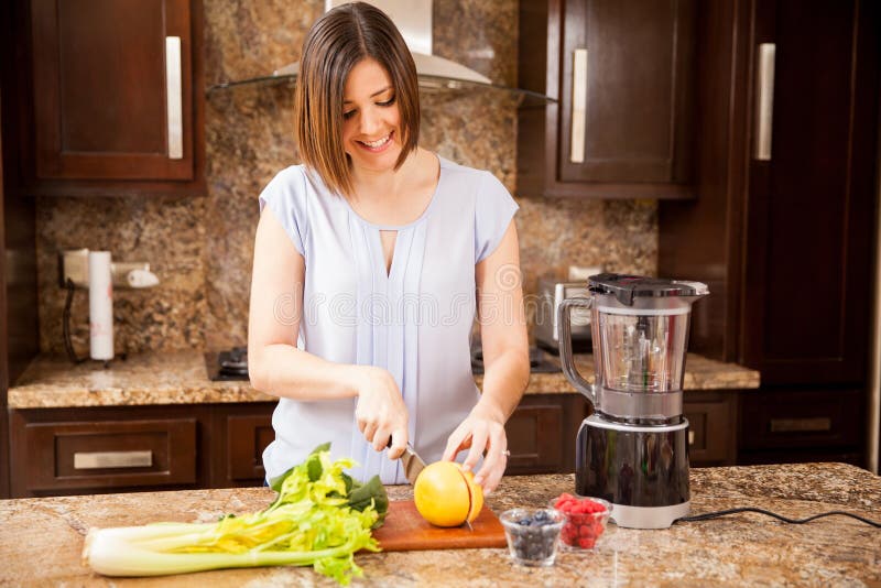 Pretty young woman cutting some fruit and vegetables to make herself a healthy juice for breakfast. Pretty young woman cutting some fruit and vegetables to make herself a healthy juice for breakfast