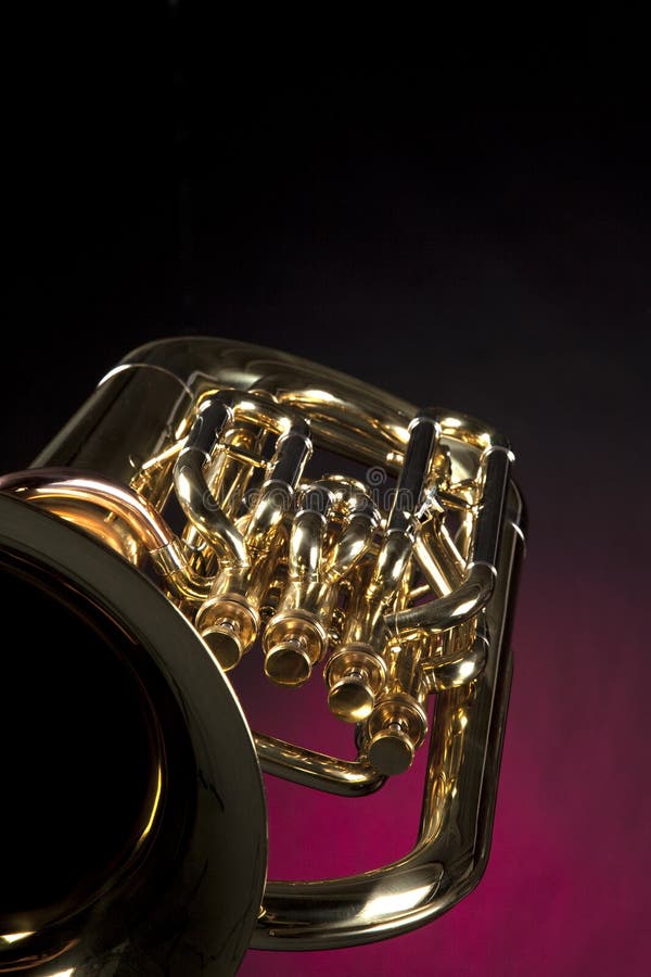 A gold brass euphonium tuba baritone isolated against a dark red background. A gold brass euphonium tuba baritone isolated against a dark red background.