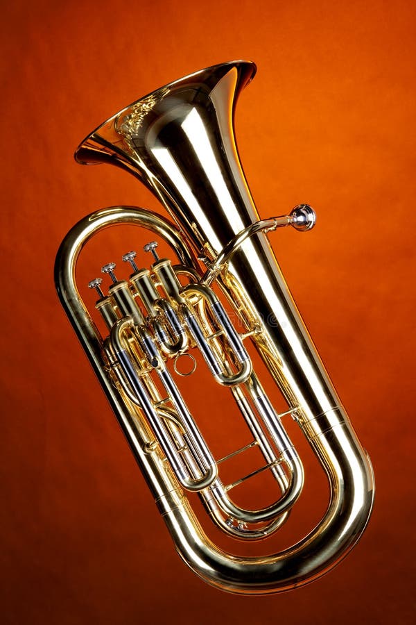 A gold Euphonium tuba baritone horn isolated against an orange background in the vertical format. A gold Euphonium tuba baritone horn isolated against an orange background in the vertical format.