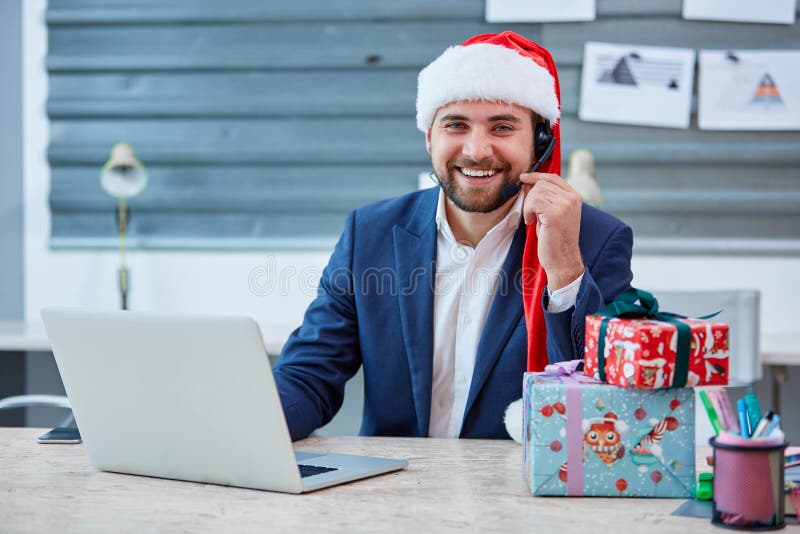 European male office worker in a Christmas hat, suit and headphones on head, sitting at desk with a laptop and laughing. royalty free stock photo European male office worker in a Christmas hat, suit and headphones on head, sitting at desk with a laptop and laughing. royalty free stock photo