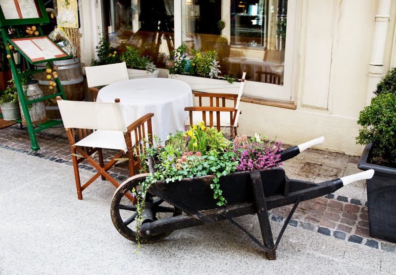 European outdoor cafe. Old wooden wheelbarrow with flowers in european outdoor cafe stock photos