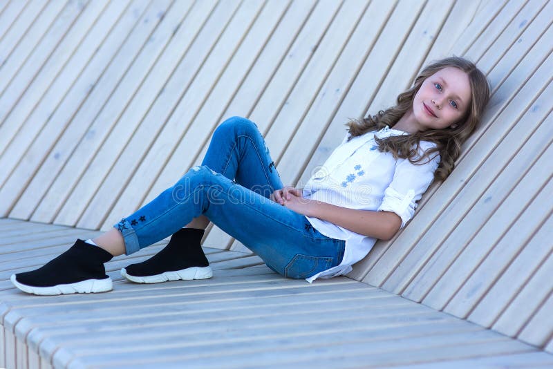 European pretty girl in fashionable clothes sits on a wooden bench outdoors. Beautiful stylish girl model enjoys relaxing in the stock image European pretty girl in fashionable clothes sits on a wooden bench outdoors. Beautiful stylish girl model enjoys relaxing in the stock image