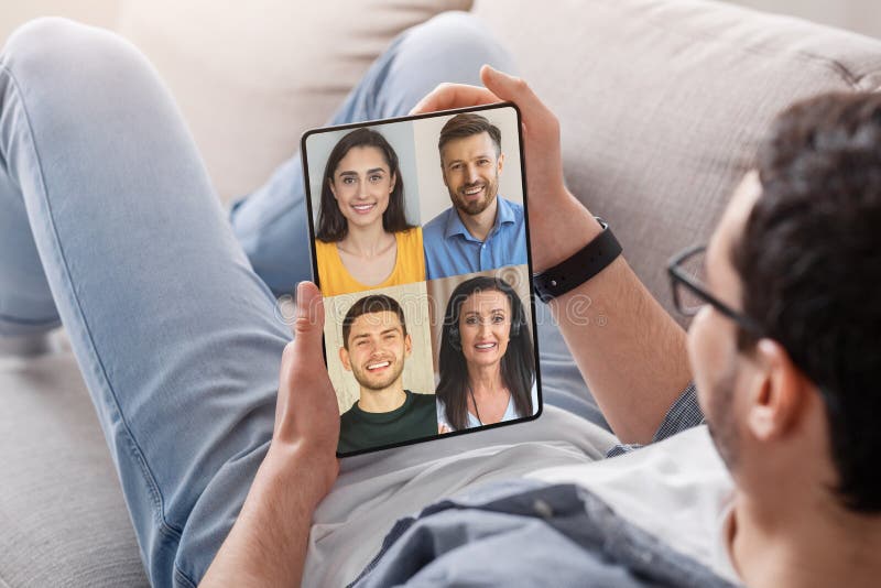 Europeen millénaire homme se reposer sur canapé avoir une réunion à distance avec des amis sur l'écran tablette photographie stock libre de droits