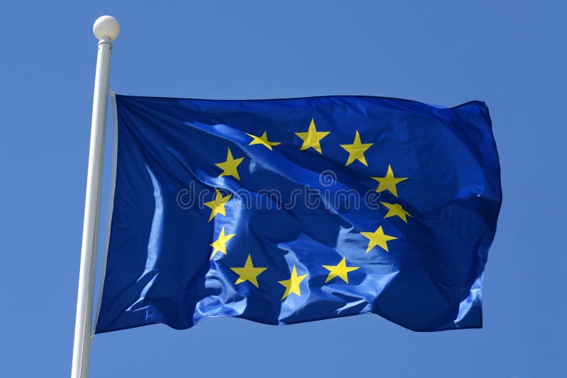 European Union flag flying from a flagpole fluttering in the breeze against a blue sky. European Union flag flying from a flagpole fluttering in the breeze against a blue sky