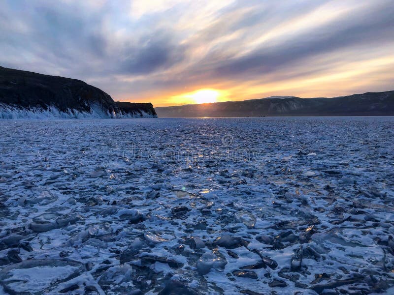 Evening view. Cracks on the surface of the blue ice. Frozen lake Baikal in winter mountains. It is snowing. The hills of pines. Ca stock images Evening view. Cracks on the surface of the blue ice. Frozen lake Baikal in winter mountains. It is snowing. The hills of pines. Ca stock images