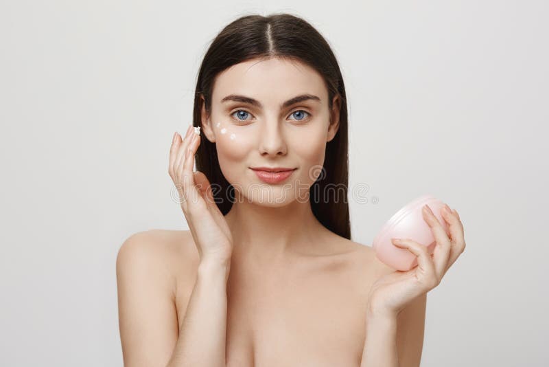 Every natural beauty needs some help. Portrait of charming blue-eyes european girl putting on facial cream, rubbing it stock photography Every natural beauty needs some help. Portrait of charming blue-eyes european girl putting on facial cream, rubbing it stock photography