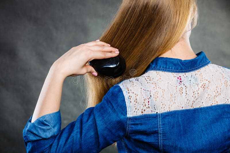Everyday hygiene and care about good look. Back view of blonde casual girl combing her long straight hair. Woman using black comb hairbrush. Everyday hygiene and care about good look. Back view of blonde casual girl combing her long straight hair. Woman using black comb hairbrush.